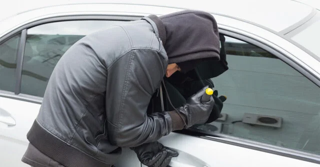 Man in black hoodie trying to break into a car with a screwdriver